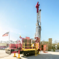 Schramm T455GT track mounted reverse circulation drill rig next to building with American flag.